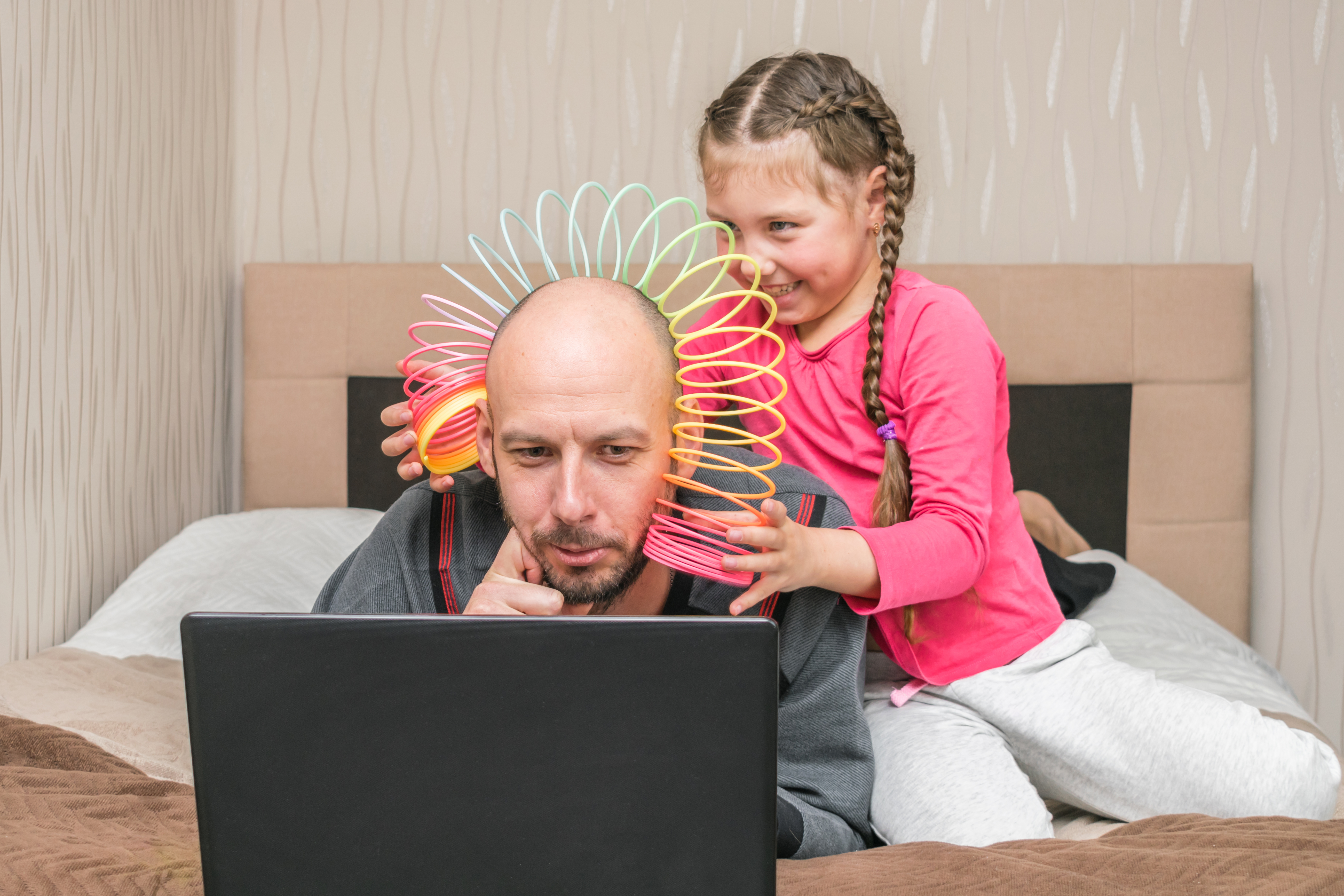 father working while daughter plays with slinky on his head