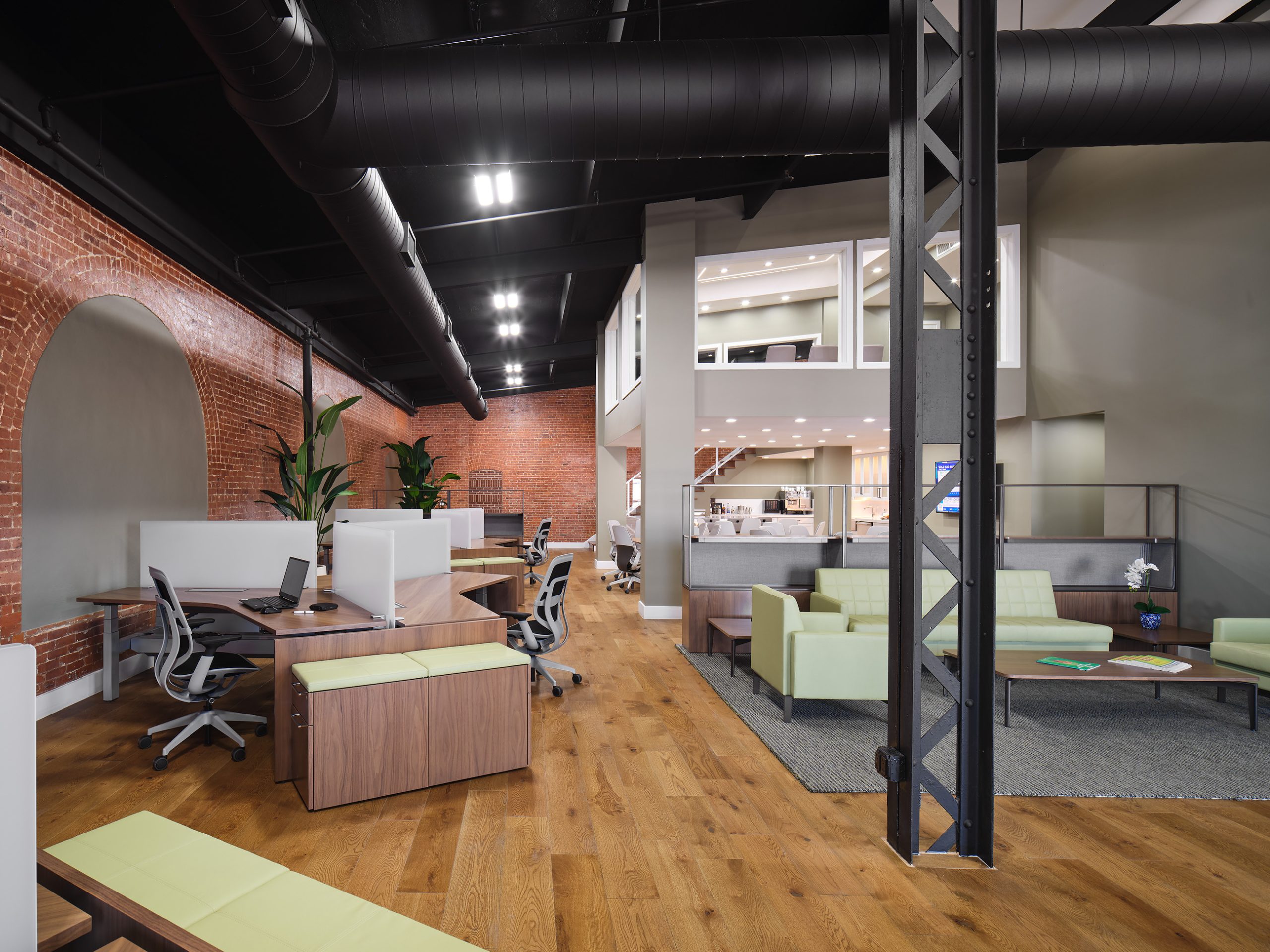 Workstations with bright green chairs in a renovated room featuring an exposed brick wall, creating a modern and vibrant workspace.